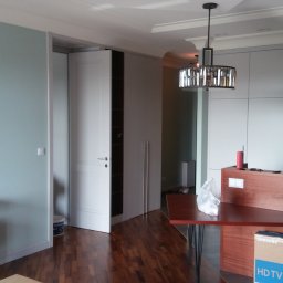 RAFAŁ POŚLEDNIAK BUD-RAF - Nowoczesne wnętrze po remoncie: błękitna ściana, zabudowa kuchenna z drewnianymi akcentami, białe drzwi do garderoby i parkiet. Widoczny karton po telewizorze.