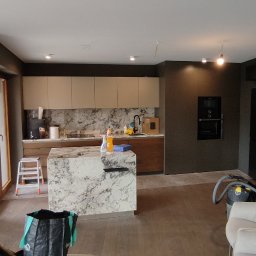 RAFAŁ POŚLEDNIAK BUD-RAF - Nowoczesna kuchnia w trakcie wykańczania: marmurowa wyspa, beżowe szafki, ciemne ściany. Widoczne narzędzia i akcesoria, sugerujące etap po remoncie, przed ostatecznym sprzątaniem.