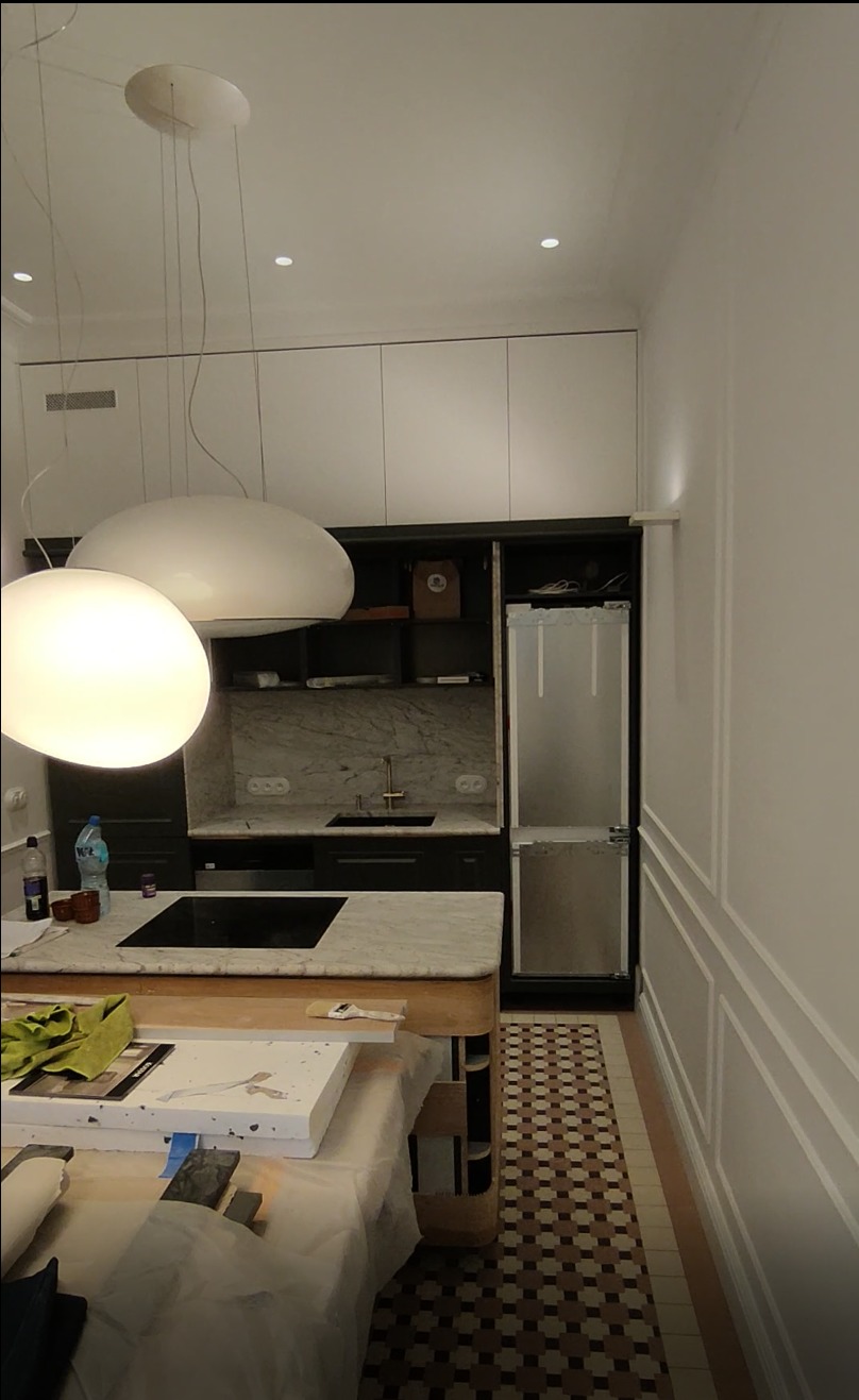 Nowoczesna kuchnia w trakcie wykańczania: marmurowy blat, białe szafki, designerskie lampy. Widoczne materiały i narzędzia na wyspie kuchennej.