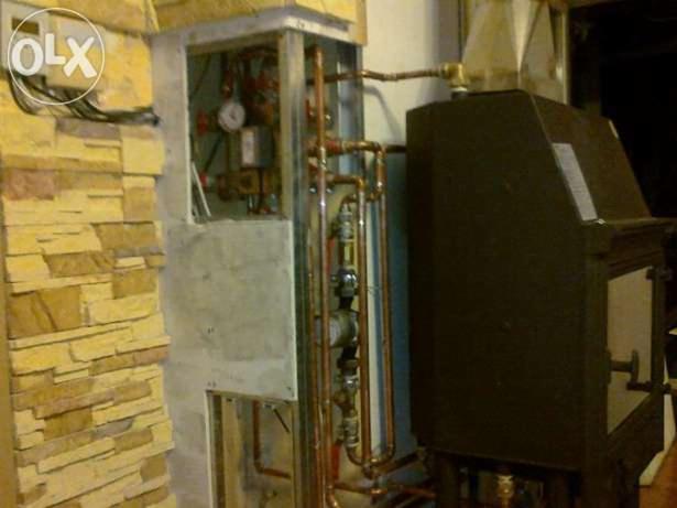 Zamontowany piec CO z widocznymi miedzianymi rurami instalacji grzewczej, obok ściana wyłożona kamieniem dekoracyjnym. Etap prac wykończeniowych.