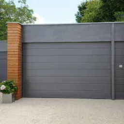 Szara segmentowa brama garażowa Hormann z poziomymi przetłoczeniami, bez napędu i przeszkleń, z prowadzeniem N, zamontowana w nowoczesnym garażu z drewnianą elewacją, widok z zewnątrz na tle...