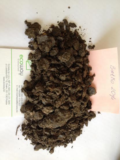 Próbka ciemnego, grudkowatego materiału organicznego z notatką 'Białko 20%' i wizytówką Ecoway, ukazująca analizę składu i identyfikację dostawcy.