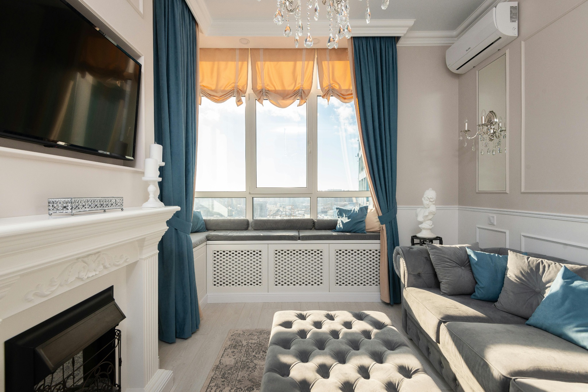 Elegancki salon z klimatyzatorem ściennym, kominkiem, szarymi zasłonami i widokiem na miasto za oknem.