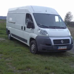 Biały bus dostawczy na trawie, z widoczną tablicą rejestracyjną KR 313XY i otoczeniem polnym w tle. Pojazd zaparkowany bokiem, z widoczną przednią częścią.