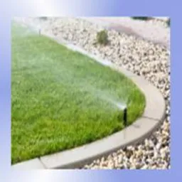 Zraszacz nawadnia soczyście zielony trawnik oddzielony betonową obwódką od kamiennego rabatu w słoneczny dzień. Precyzyjne nawadnianie.