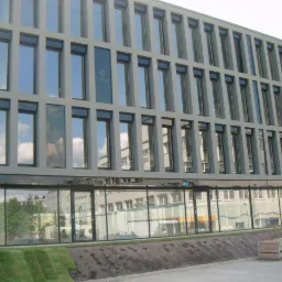 Elewacja biurowca Garden Plaza w Warszawie z licznymi oknami, odbijającymi niebo i chmury, na pierwszym planie trawnik i paleta.