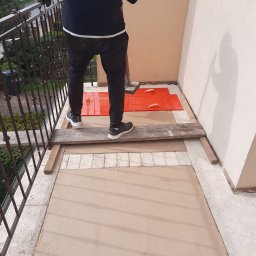 Zakład Remontowo-Budowlany - Balkon w trakcie prac: świeżo wylana, beżowa posadzka, zabezpieczona część podłoża. Widoczne narzędzia i fragment osoby wykonującej prace.