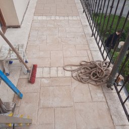 Zakład Remontowo-Budowlany - Balkon z nową, beżową posadzką imitującą kamień. Widoczne narzędzia: drabina, szczotka, sznurek. Metalowa balustrada i fragment elewacji w tle.