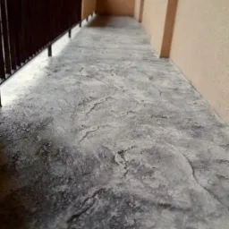 Szara posadzka mikrocementowa na balkonie, imitująca kamień naturalny, z widoczną balustradą i ścianą w odcieniach beżu.