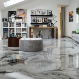 Wnętrze salonu z błyszczącą, szarą posadzką żywiczną z efektem marmuru, szary puf na pierwszym planie, w tle regał z książkami, drewniane biurko i szara sofa.