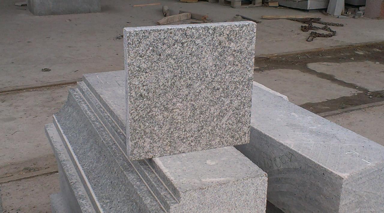 Granitowe płyty chodnikowe w odcieniach szarości, ułożone na palecie w magazynie budowlanym, z widoczną fakturą kamienia.