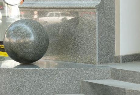 Granitowa kula dekoracyjna na tle schodów z granitu o drobnej fakturze. Widoczny fragment ściany i odbicie samochodu w polerowanej powierzchni granitu.