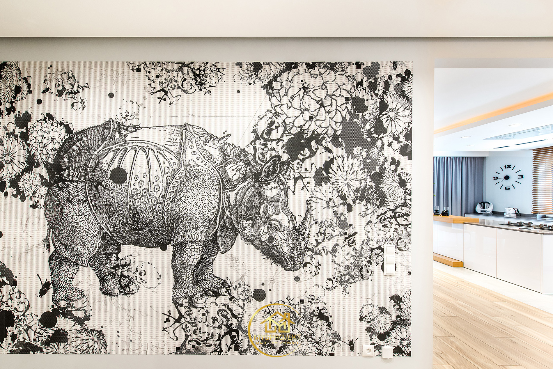 Czarno-biała fototapeta z motywem nosorożca i kwiatów w nowoczesnej kuchni z białymi meblami i drewnianą podłogą. Widok na wnętrze przez otwarte przejście.
