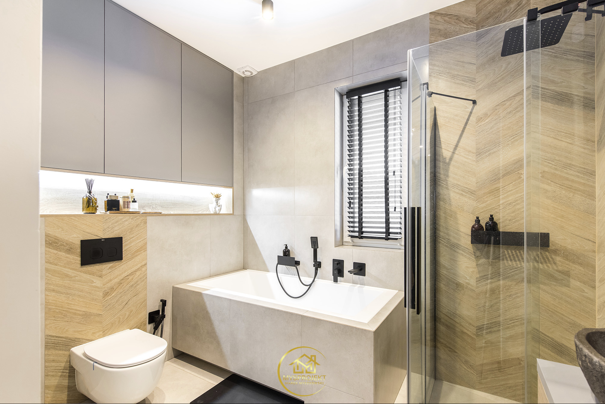 Nowoczesna łazienka z wanną, kabiną prysznicową typu walk-in i toaletą podwieszaną. Uwagę zwracają płytki imitujące drewno ułożone w jodełkę i czarna armatura.
