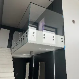 Szklana balustrada na antresoli z czarnymi punktami mocującymi, widoczne schody i oświetlenie LED w nowoczesnym wnętrzu.