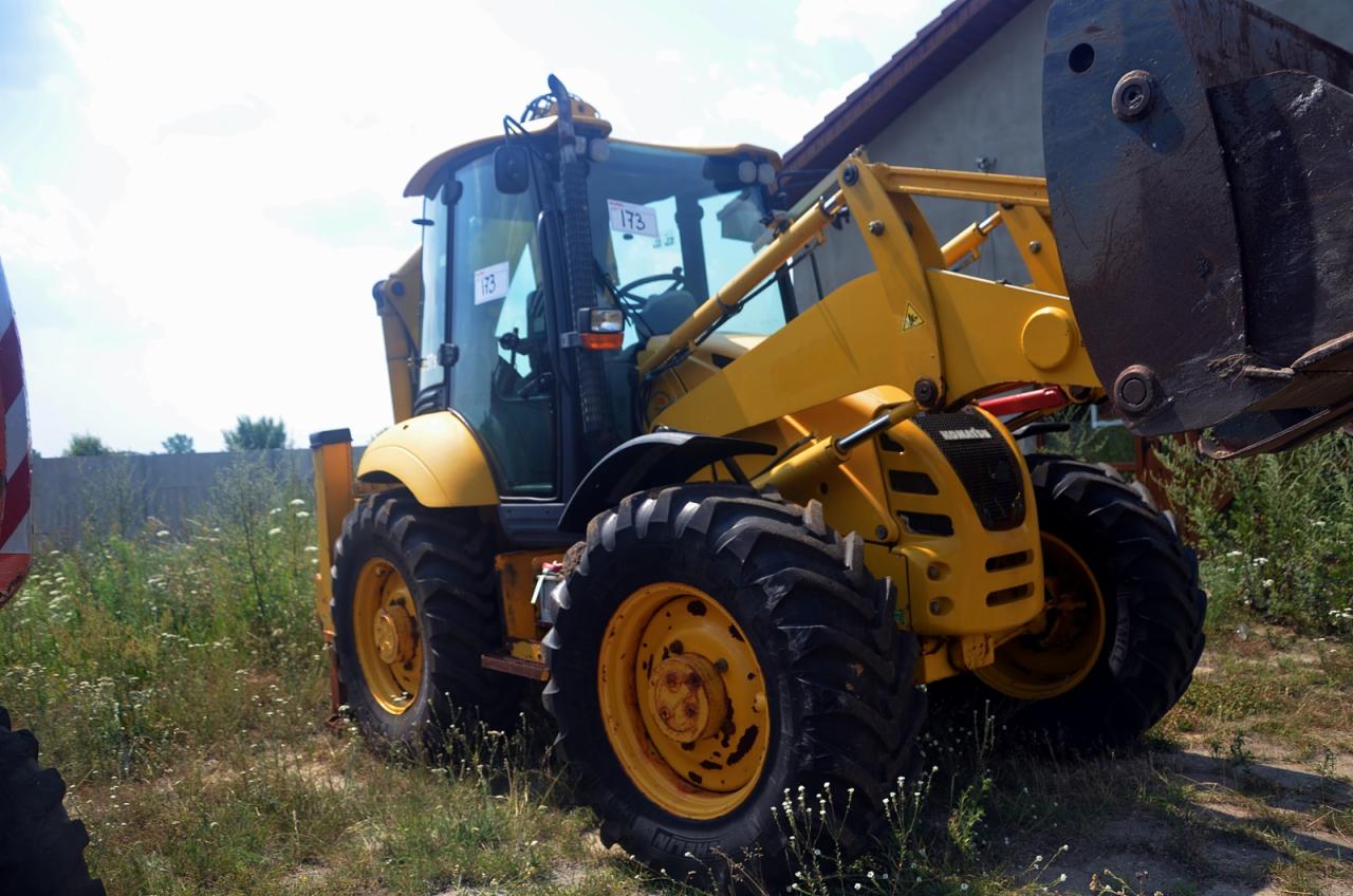 Żółta koparko-ładowarka Komatsu W97S-5 na trawiastym terenie, widoczne numery identyfikacyjne na szybach kabiny.