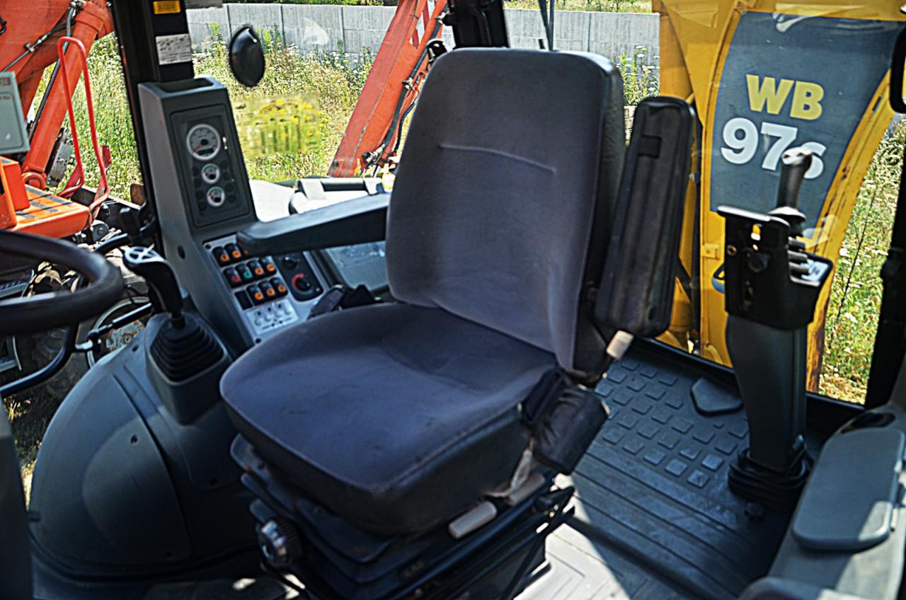 Wnętrze kabiny Komatsu W97S-5: fotel operatora, panel sterowania z przełącznikami, dźwignie i widoczny fragment ramienia koparki za szybą.
