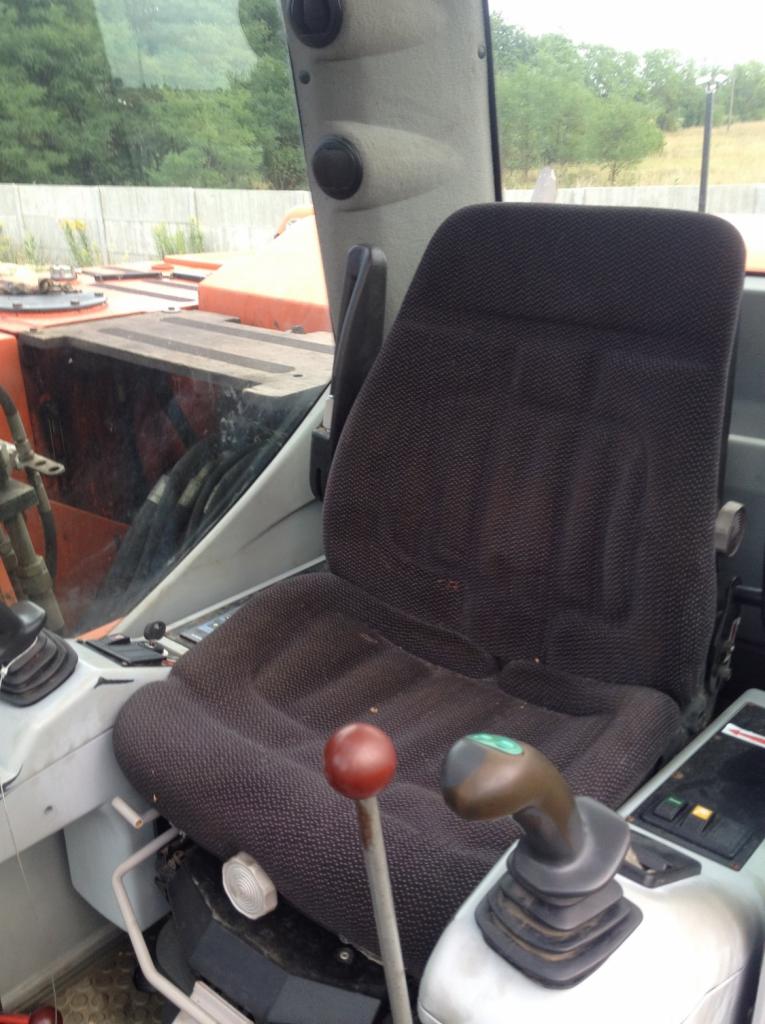 Wnętrze kabiny maszyny budowlanej, fotel operatora z widocznymi elementami sterującymi i szybą przednią.