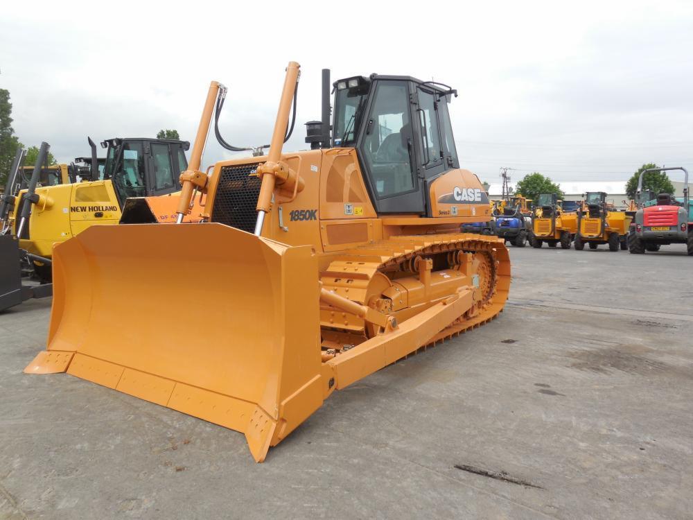 Pomarańczowy spychacz Case 1850K na placu z innymi maszynami budowlanymi w tle.