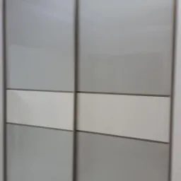 Dwudrzwiowa szafa wnękowa z przesuwnymi drzwiami w odcieniach szarości i bieli, widoczna z bliska, z dekoracyjnym żyrandolem na suficie