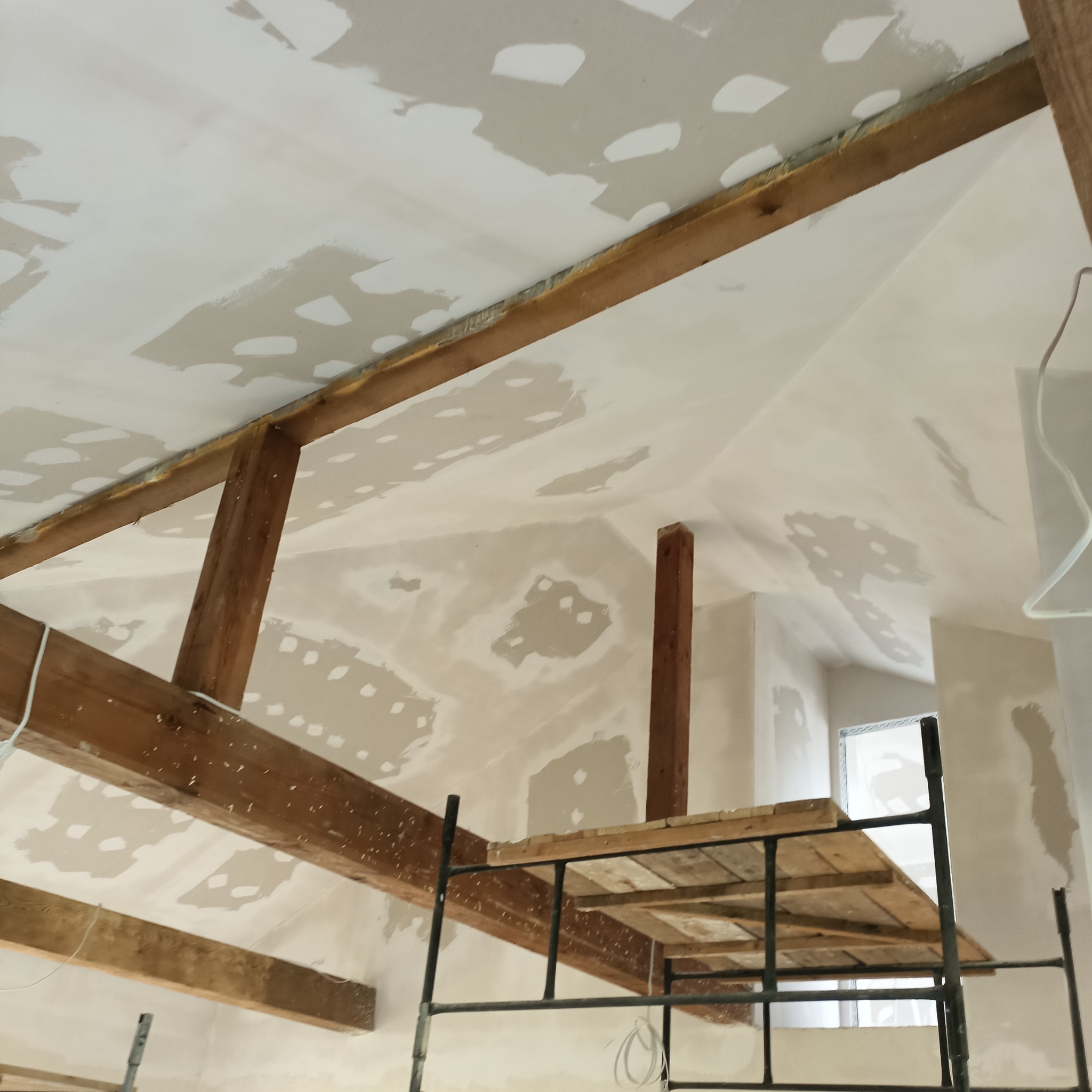 Skośny sufit z drewnianymi belkami w trakcie szpachlowania, widoczny fragment rusztowania.