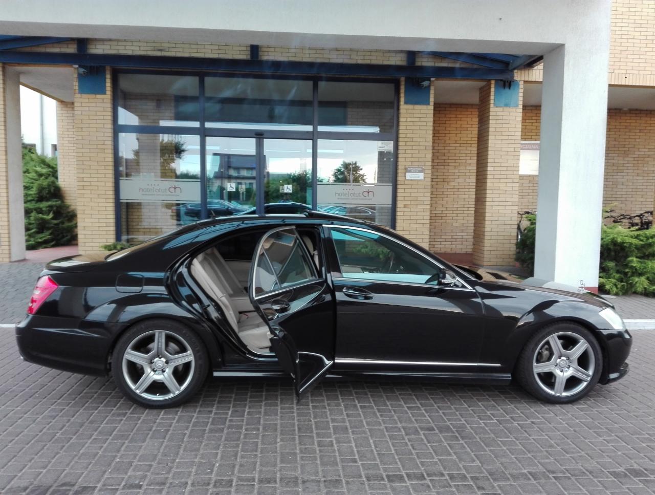 Czarna limuzyna Mercedes z otwartymi drzwiami na tle wejścia do hotelu z cegły.