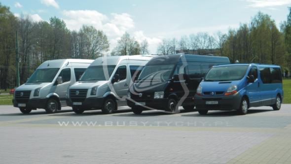 Rząd czterech busów różnych marek i kolorów (biały, srebrny, czarny, niebieski) ustawionych na parkingu z drzewami w tle, widoczne logo firmy na szybie jednego z pojazdów.