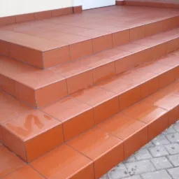 Zewnętrzne schody wejściowe wyłożone terakotą w odcieniach pomarańczy, z widocznymi śladami wilgoci na powierzchni płytek.