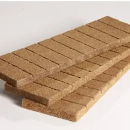 Ułożone warstwami prostokątne brykiety węglowe o jednolitej strukturze i brązowym odcieniu, widoczne delikatne pęknięcia na powierzchni jednego z brykietów.