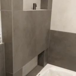 Wykończona wnęka w szarej glazurze nad wanną, zabezpieczoną folią, w łazience w Starogardzie Gdańskim. Na półce wnęki stoi pojedynczy, metalowy przedmiot.