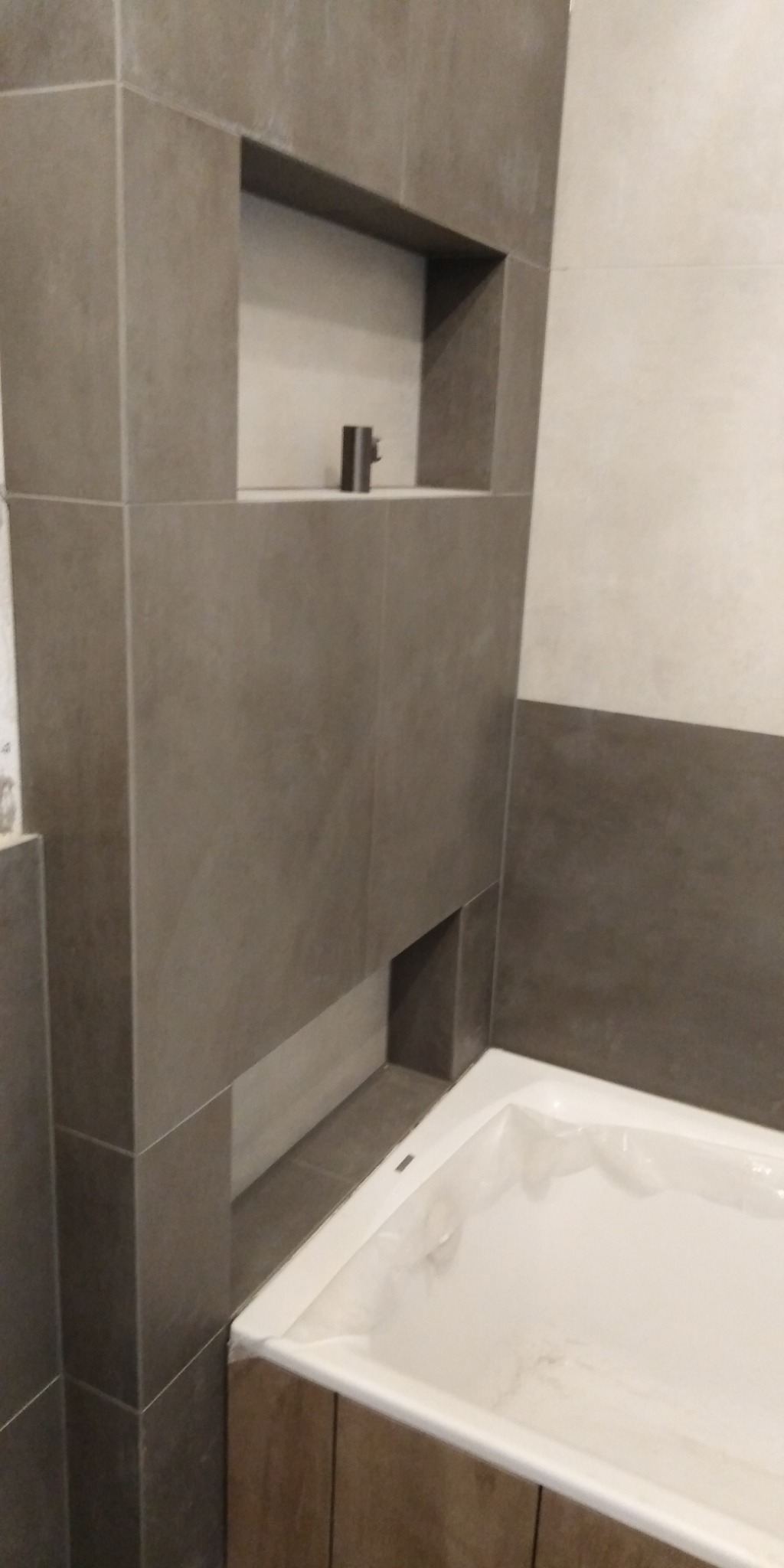 Wykończona wnęka w szarej glazurze nad wanną, zabezpieczoną folią, w łazience w Starogardzie Gdańskim. Na półce wnęki stoi pojedynczy, metalowy przedmiot.