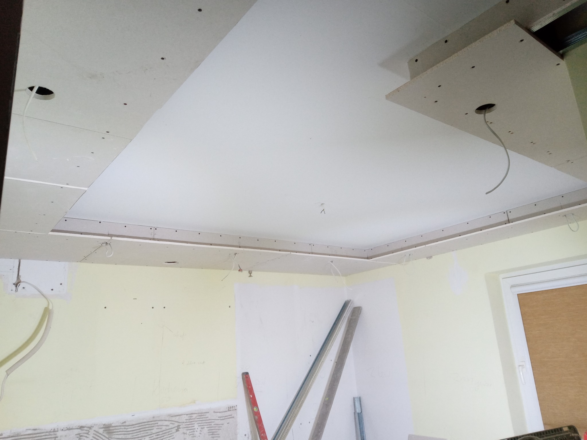 Sufit podwieszany z płyt gipsowo-kartonowych w trakcie montażu, widoczne kable oświetleniowe, ściany przygotowane do malowania, poziomice oparte o ścianę.
