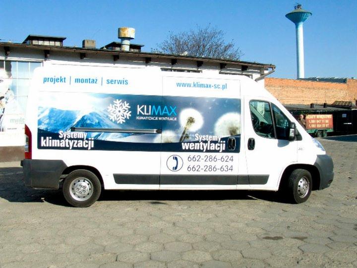 Biały furgon z grafiką firmy Klimax: klimatyzacja i wentylacja. Projekt, montaż, serwis. Widoczny numer telefonu i adres strony. W tle wieża ciśnień.