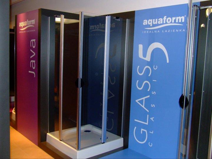 Ekspozycja kabin prysznicowych Aquaform: model Java na fioletowym tle i Glass 5 Classic na błękitnym. Srebrne ramy kabin, białe brodziki. Widok z boku, oświetlenie ekspozycyjne.