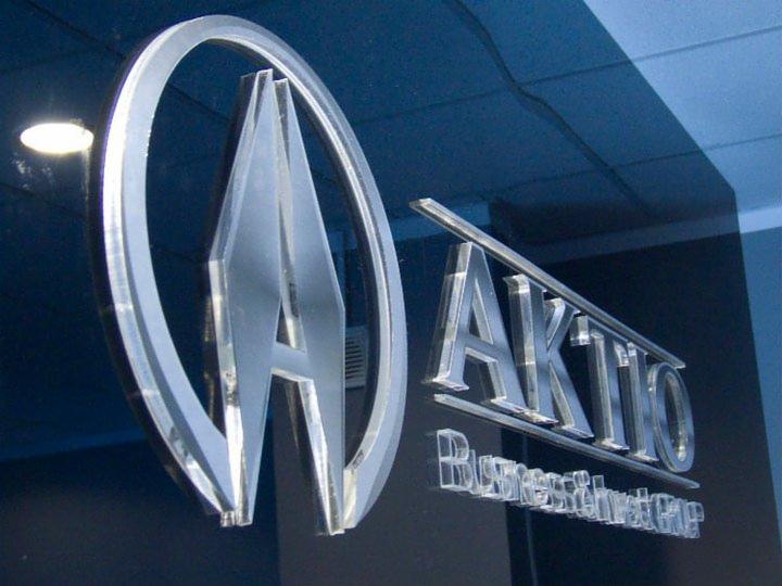 Elegancki, przestrzenny logotyp 'AKTIO' z efektem 3D, umieszczony na ciemnym tle. Wyraźne, srebrne litery i okrągły symbol nadają nowoczesny wygląd.