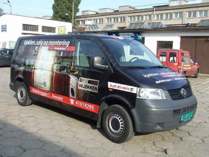 Czarny van z grafiką kuchni i logo BRW Kjokken, promujący sprzedaż i montaż kuchni, z numerem telefonu i adresem, zaparkowany na zewnątrz budynku.