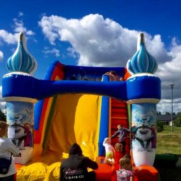 Plenerparty - Kolorowy dmuchany zamek z motywem Frozen, dzieci bawiące się na zjeżdżalni i schodach, niebieskie niebo z chmurami w tle.