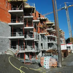 Wielorodzinny budynek mieszkalny w trakcie budowy, widoczne rusztowania, dźwig budowlany, mieszalnik do betonu i materiały budowlane Lafarge.