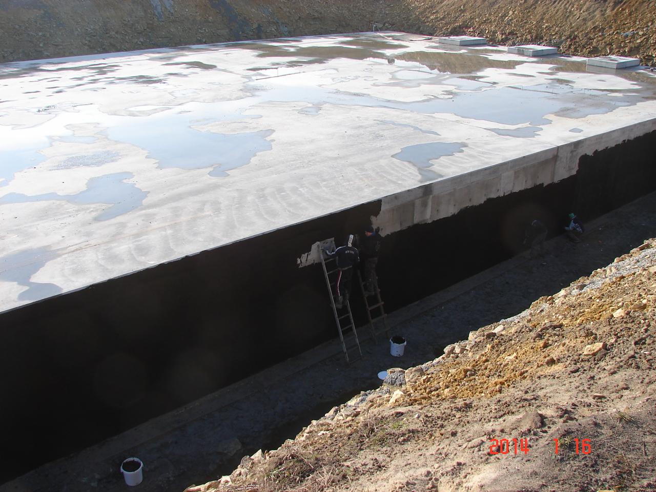 Hydroizolacja betonowej konstrukcji podziemnej z użyciem drabiny. Prace wykonywane przez dwóch pracowników. Widoczne wiaderka z materiałem izolacyjnym.