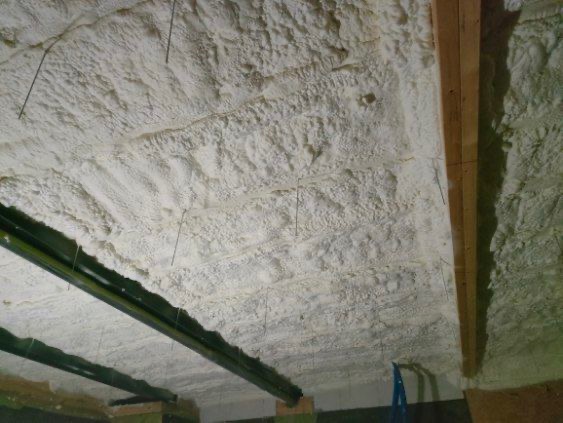 Izolacja poddasza pianką PUR z widocznymi elementami konstrukcyjnymi dachu i wystającymi drutami montażowymi.