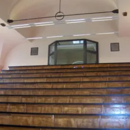 Sala audytoryjna z drewnianymi ławkami amfiteatralnymi i schodami z oświetleniem LED, widok od dołu, wysokie sklepienie z oknem łukowym.