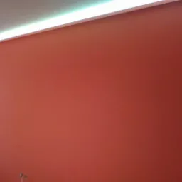 Ściana pomalowana na intensywny odcień pomarańczy, z subtelnym oświetleniem LED w listwie przysufitowej, widok na okno balkonowe z lewej strony, gniazdka elektryczne przy podłodze.