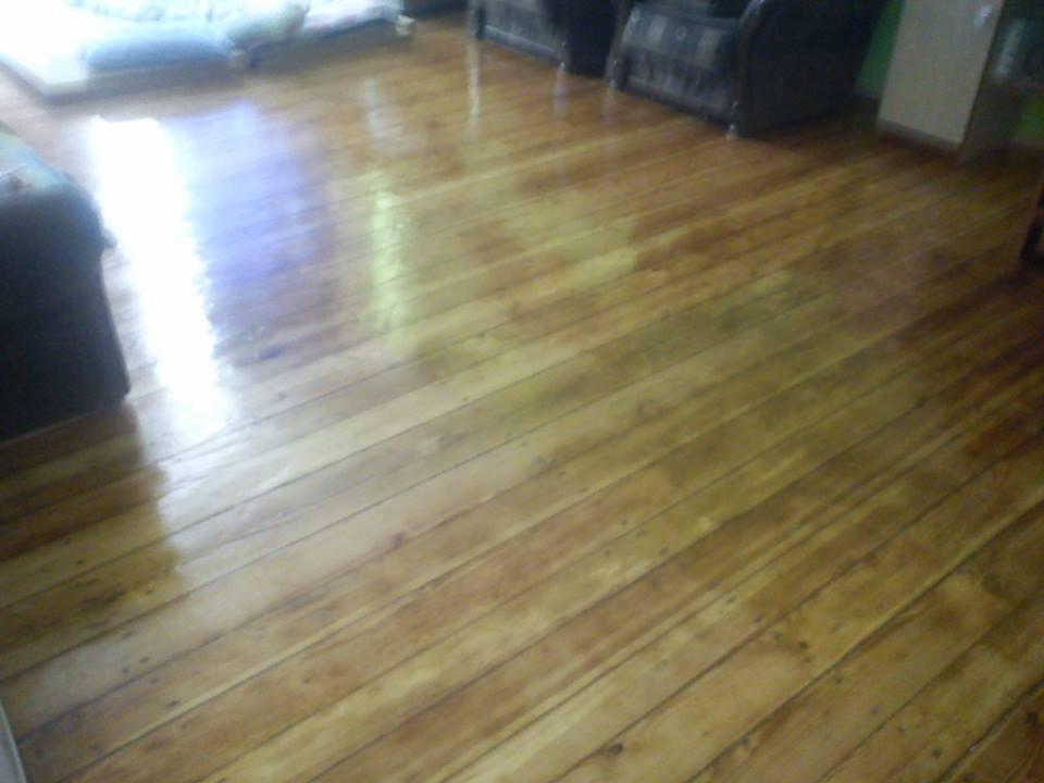 Błyszcząca, odnowiona drewniana podłoga po cyklinowaniu, z widocznymi refleksami światła i elementami wyposażenia wnętrza w tle.