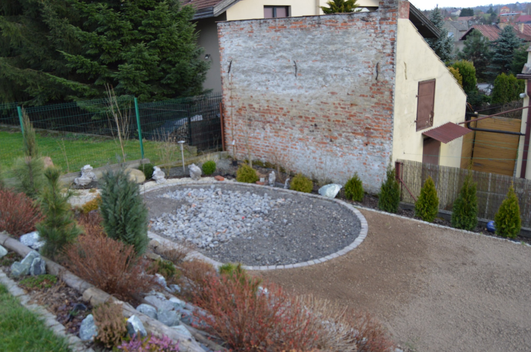 Przygotowane miejsce pod basen z kamienia naturalnego, otoczone roślinami i kamieniami ozdobnymi. Widok z góry na teren z elementami architektury ogrodowej.