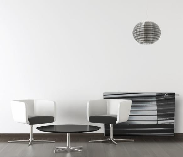 Biało-czarne fotele i okrągły stolik na tle ściany z grzejnikiem dekoracyjnym i lampą wiszącą. Minimalistyczne wnętrze.