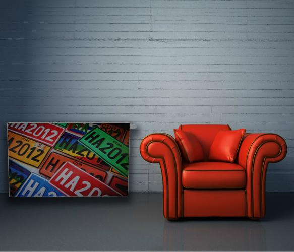 Grzejnik dekoracyjny z motywem tablic rejestracyjnych obok czerwonego fotela na tle szarej ściany. Nietypowe rozwiązanie grzewcze do salonu.