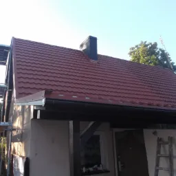 Nowy, bordowy dach z blachodachówki i czarny komin na domu w Mieszkowicach, widoczne rusztowanie i drabina.