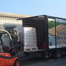 Wózek widłowy Linde ładuje paletę z towarem owiniętą folią do samochodu dostawczego z reklamą opału drzewnego na boku.