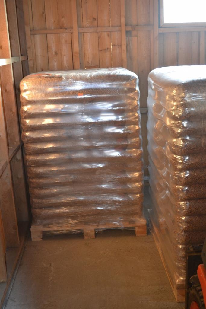 Dwa stosy worków z granulatem, owinięte folią stretch, ułożone na paletach w magazynie z drewnianymi ścianami.