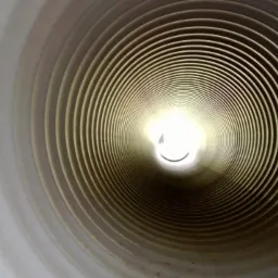 Wnętrze rury kanalizacyjnej z widocznym światłem na końcu, ukazujące perspektywę i konstrukcję instalacji. Widoczne pierścienie i faktura tworzywa.